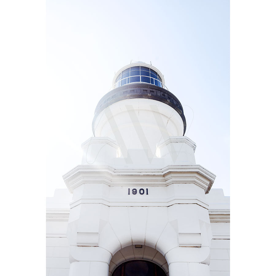 The Byron Bay Lighthouse Image 8424 by AWP Image Library captures a low-angle view of a white lighthouse with a black band near the top and windows, prominently displaying 1901. The bright, clear sky enhances its beauty.