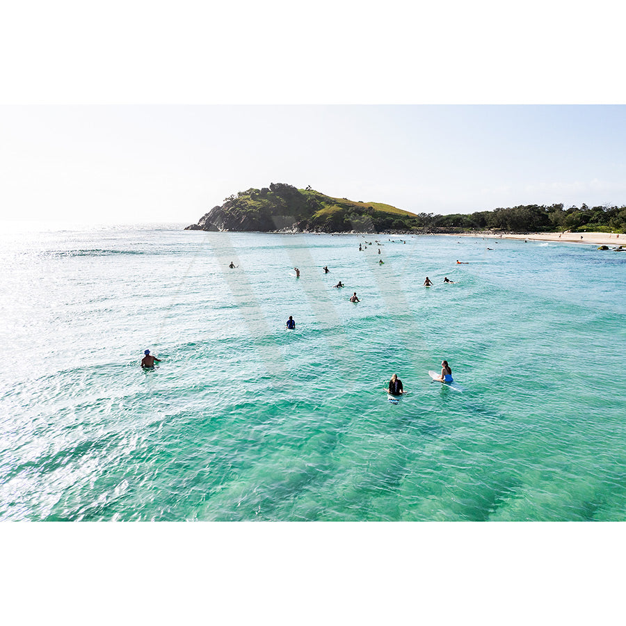 The Cabarita Beach Drone Image 0194 by AWP Image Library captures surfers and paddleboarders gliding in a turquoise ocean near a lush, green hill. The distant shoreline of Cabarita Peninsula completes the serene coastal scene under a clear blue sky.