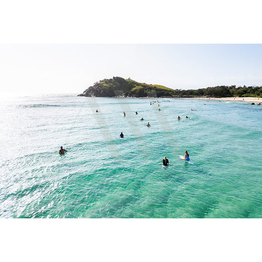 The Cabarita Beach Drone Image 0194 by AWP Image Library captures surfers and paddleboarders gliding in a turquoise ocean near a lush, green hill. The distant shoreline of Cabarita Peninsula completes the serene coastal scene under a clear blue sky.