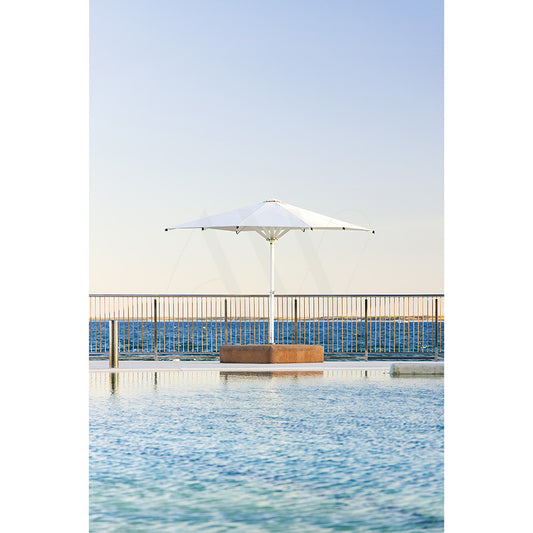 Kings Beach Pool Image 8288 by AWP Image Library shows a white umbrella next to the family-friendly pool at Kings Beach, bordered by a metal railing with stunning ocean and clear sky views in the background.