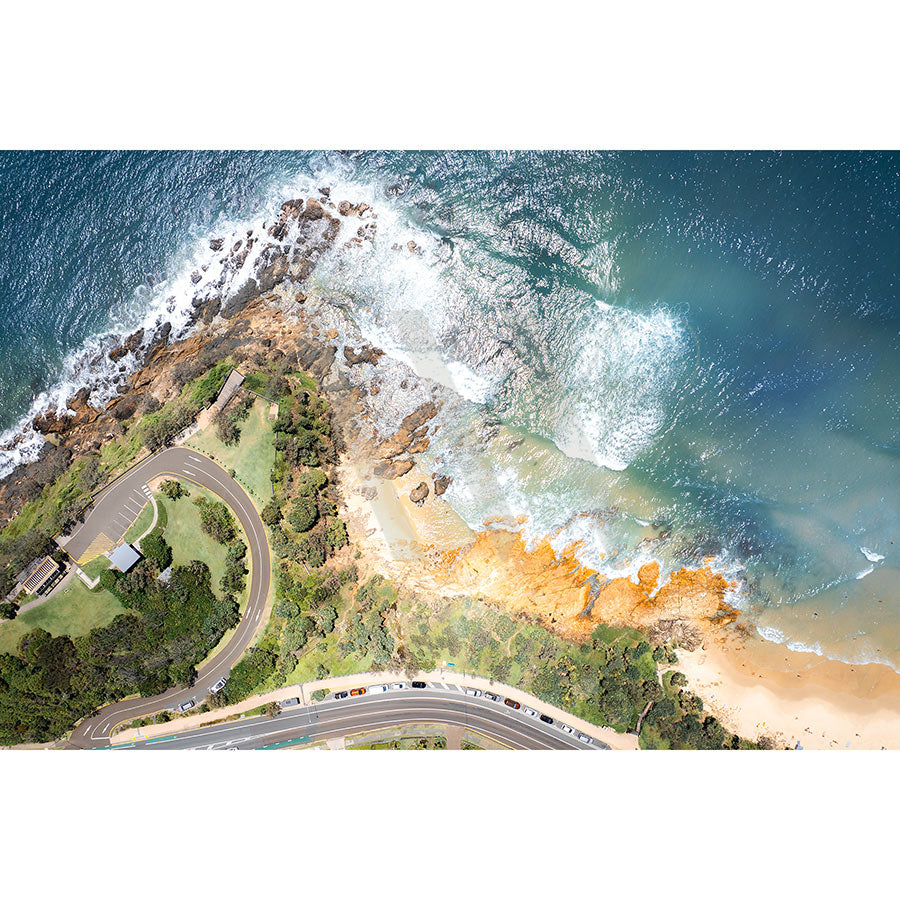 Coolum Beach Drone Image 0111 by AWP Image Library showcases a stunning aerial view of Coolum Beach with golden sand, rocky outcrops, clear blue waters, and a curving road lined with greenery. Waves gently crash against the rocks and shore, creating a stairway to paradise.