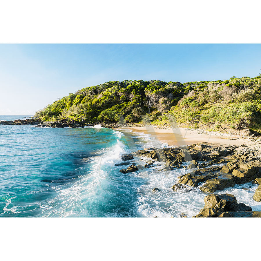 The Coolum Beach Drone Image 0257 from AWP Image Library captures a rocky beach with turquoise waves and lush green hills beneath a clear blue sky.