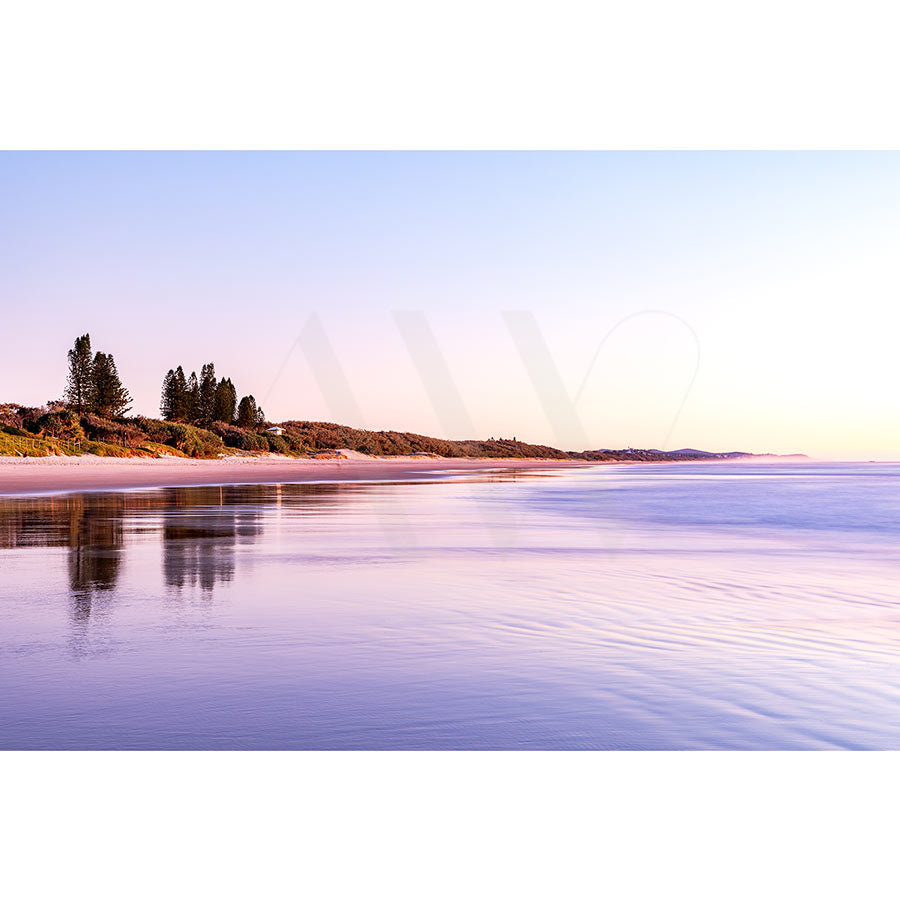 The Coolum Beach Image 8724 from AWP Image Library depicts a serene sunrise beach scene with calm waves, light sand stretching along the coast, distant trees, and a clear sky with pastel hues reflecting on the water.