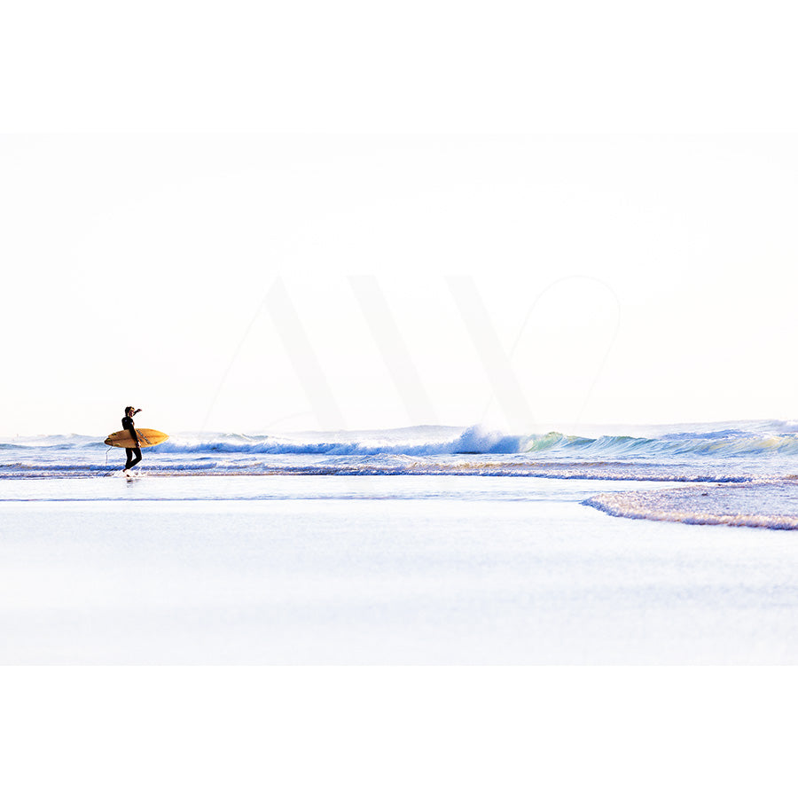 Coolum Beach Surfer Image 9075 by AWP Image Library captures a serene scene with a lone surfer carrying a yellow surfboard along the beach, set against a bright sky and gentle waves.