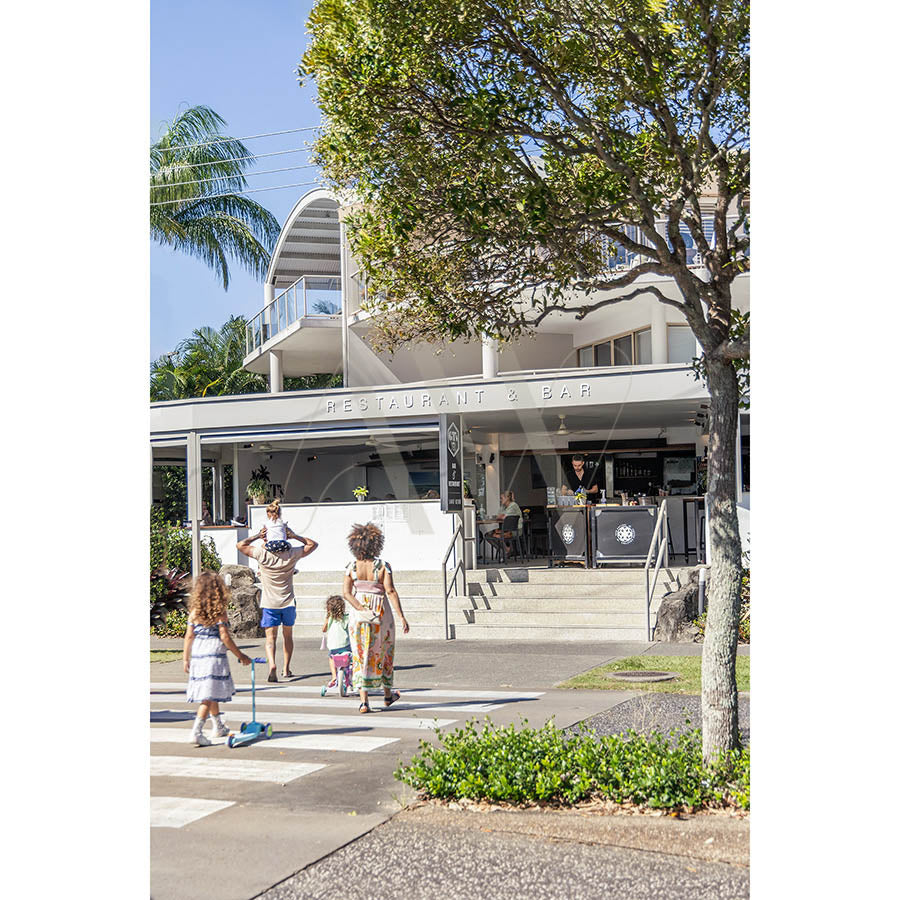 A family with children crosses a sunny street toward Depot Coffee Shop, surrounded by greenery, as a child scooters in front—captured in Gympie Tce Image 3947 by AWP Image Library. Perfect for brunch or coffee with loved ones.