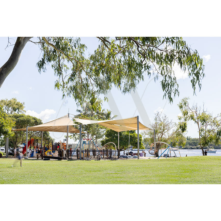 The AWP Image Librarys Gympie Tce Image 4800 shows a grassy playground with modern equipment and shade sails near the Noosa River, surrounded by trees, parked cars, and children playing under a mostly clear sky.