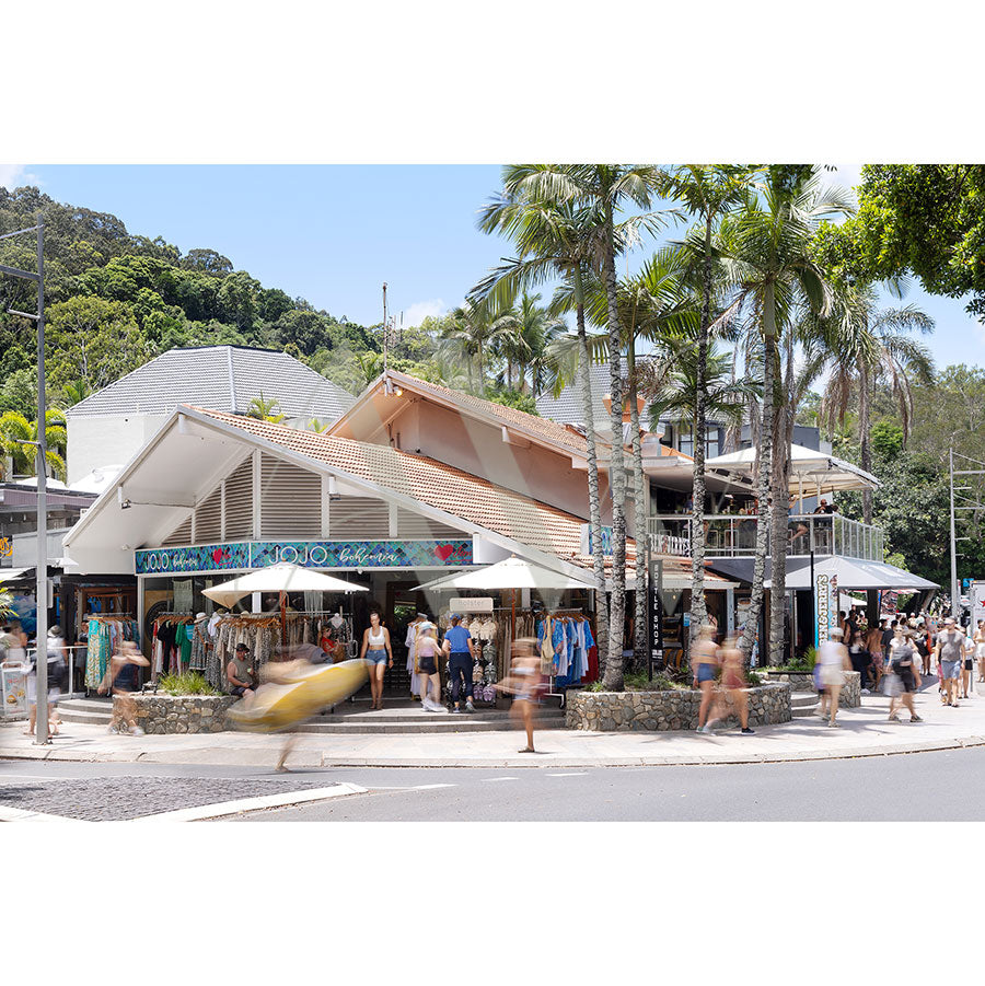 The vibrant Hastings Street Image 5541 by AWP Image Library captures a bustling two-story shopping area with cafes, people in motion blur, palm tree-lined sidewalks, and brightly colored clothing displayed under large umbrellas.