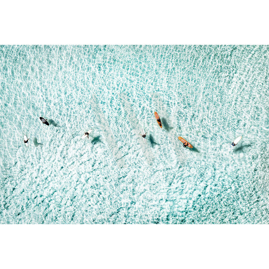 The Noosa Drone Image 0736 by AWP Image Library captures an aerial view of seven surfers paddling in clear turquoise water, creating gentle ripples. Spaced diagonally, the sunlight highlights the waters texture beautifully.