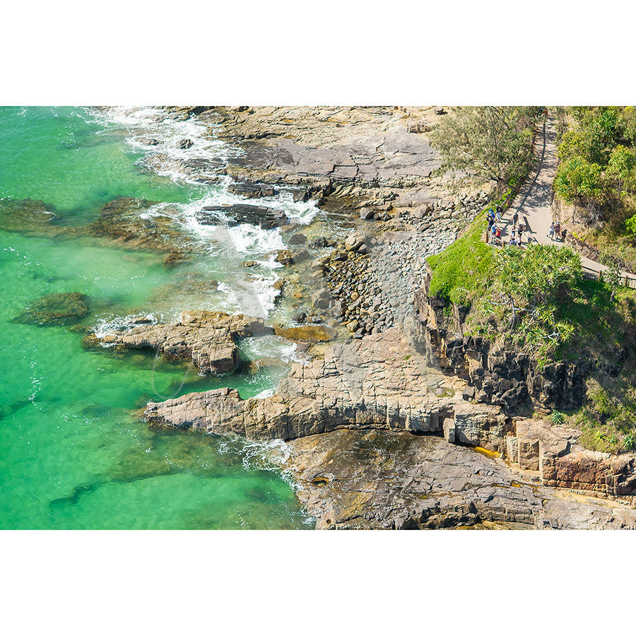 A group overlooks turquoise waters and a rugged coastline from a rocky cliff at Main Beach in the Noosa National Park Drone Image 1346 by AWP Image Library.