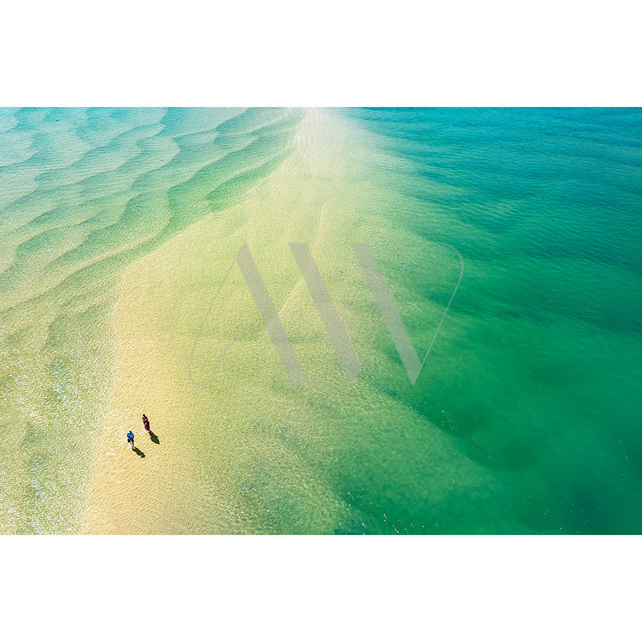 The Noosa River Drone Image 0857 by AWP Image Library captures an aerial view of two people walking on a sandbar amidst turquoise and emerald waters, with light reflections creating ripple patterns that blend seamlessly with the sandy shore.