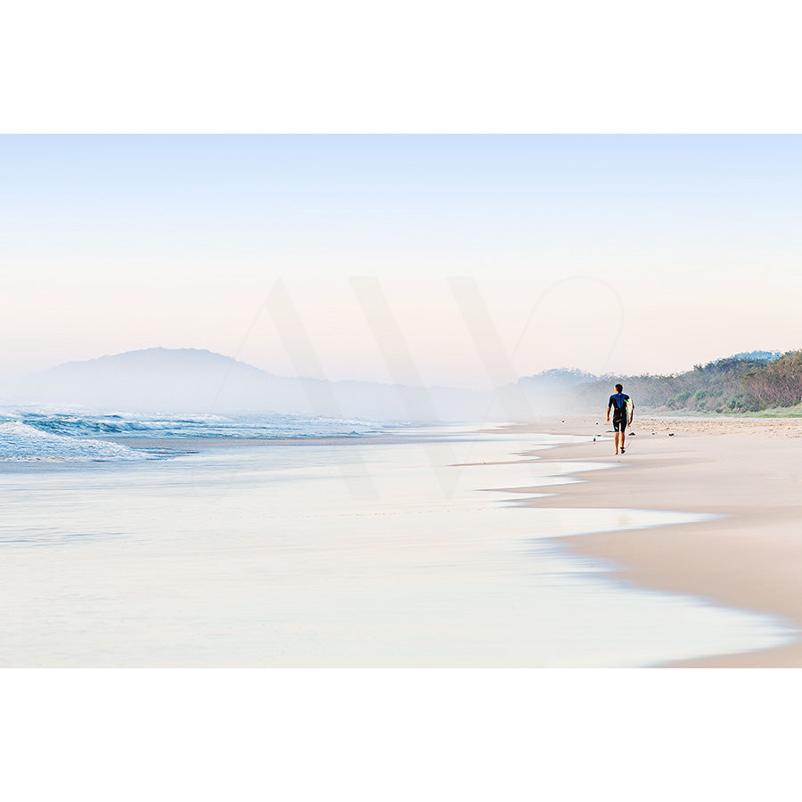 Ocean Shores Image 7994 by AWP Image Library captures a jogger on a tranquil, empty beach beneath a pale blue sky. Gentle waves touch the shore, with faint hills in the background, evoking calm and solitude.