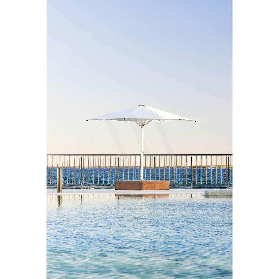 Kings Beach Pool Image 8288 by AWP Image Library shows a white umbrella next to the family-friendly pool at Kings Beach, bordered by a metal railing with stunning ocean and clear sky views in the background.