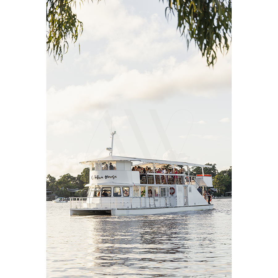 Gympie Tce Image 3368 from AWP Image Library features a white, two-level party boat cruising a calm river, surrounded by trees and partly cloudy skies, with overhanging branches in view.