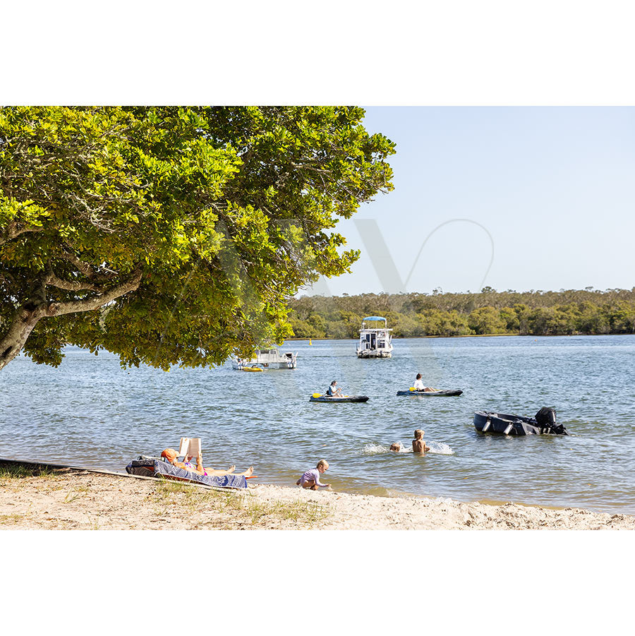 The AWP Image Librarys Gympie Tce Image 3785 shows people relaxing under a large tree on Noosa’s sandy foreshore, while others kayak and swim in calm waters, with small boats and kayaks near the forested Gympie Terrace shoreline.