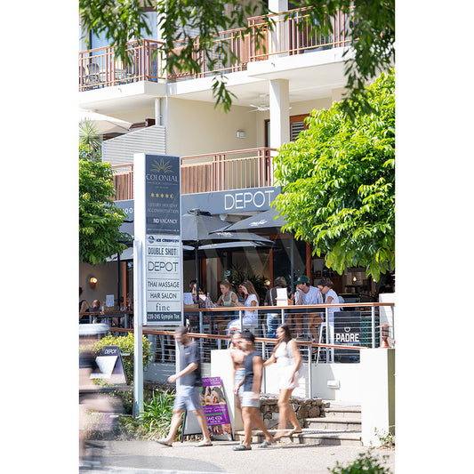 AWP Image Librarys Gympie Tce Image 4451 captures a lively street scene near Noosa River, with couples at outdoor Depot café tables, passersby, green trees framing a modern building, and signage for local businesses like massage and hair salons.